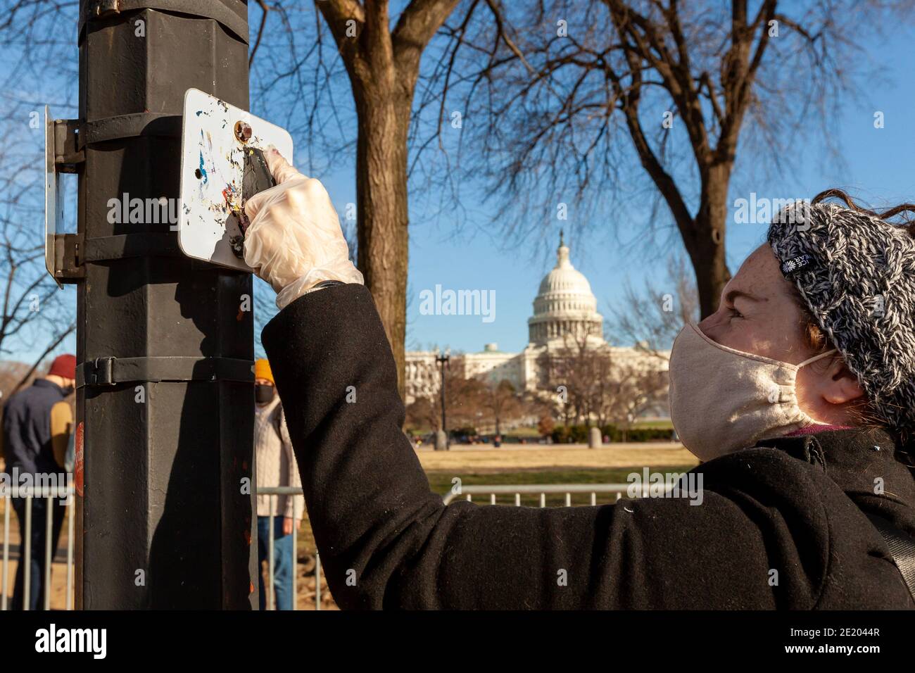 Washington, DC, USA, 10 January 2021.  Pictured:  A volunteer scrapes stickers stickers off a sign near the Capitol during Operation Clean Sweep. The event was an effort to clean up trash and propaganda left behind by fascists and Trump supporters following the January 6 Capitol insurrection. It was hosted by Continue to Serve, an anti-racist organization of military veterans.  Credit: Allison C Bailey/Alamy Live News Stock Photo