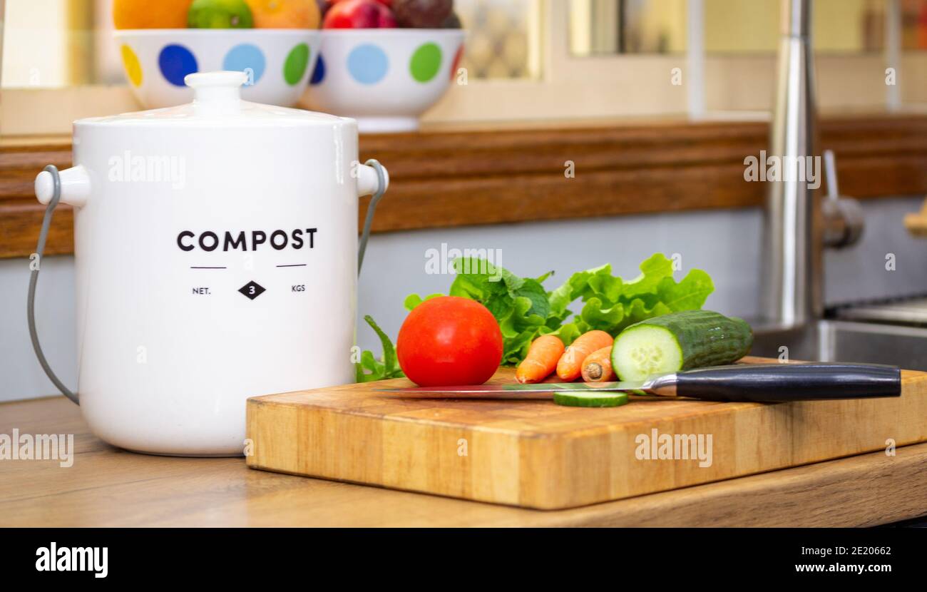 close up of recycle food waste kitchen compost container with chopped vegetables and knife on chopping board, sustainable living concept Stock Photo
