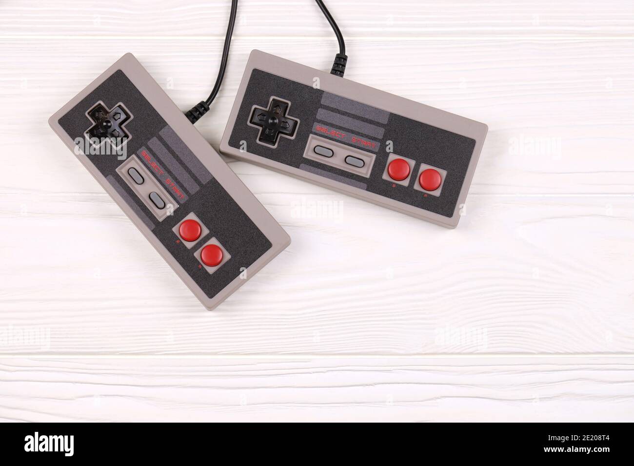 KHARKOV, UKRAINE - DECEMBER 27, 2020: Two old gamepads for 8-bit video game consoles nintendo entertainment system and nes mini on white wooden table. Stock Photo