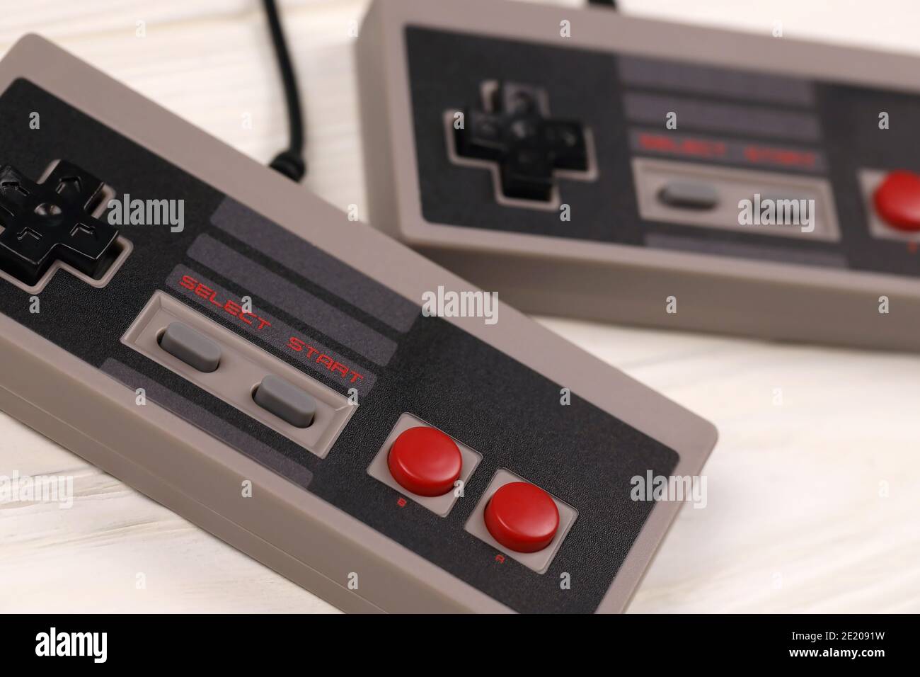 KHARKOV, UKRAINE - DECEMBER 27, 2020: Two old gamepads for 8-bit video game consoles nintendo entertainment system and nes mini on white wooden table. Stock Photo