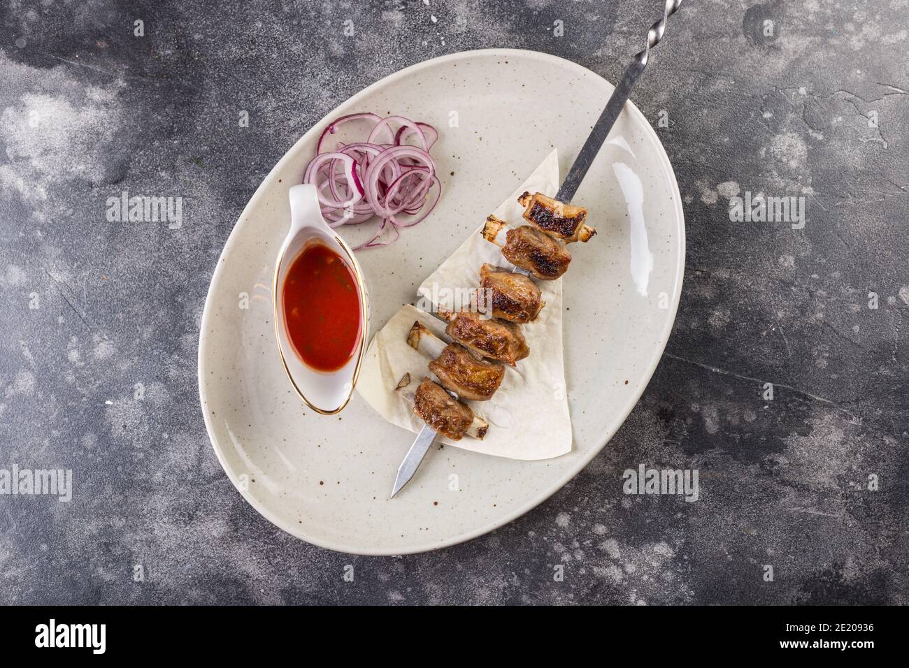 Delicious pork shashlik on a plate with tomato sauce and onions. Top view Stock Photo