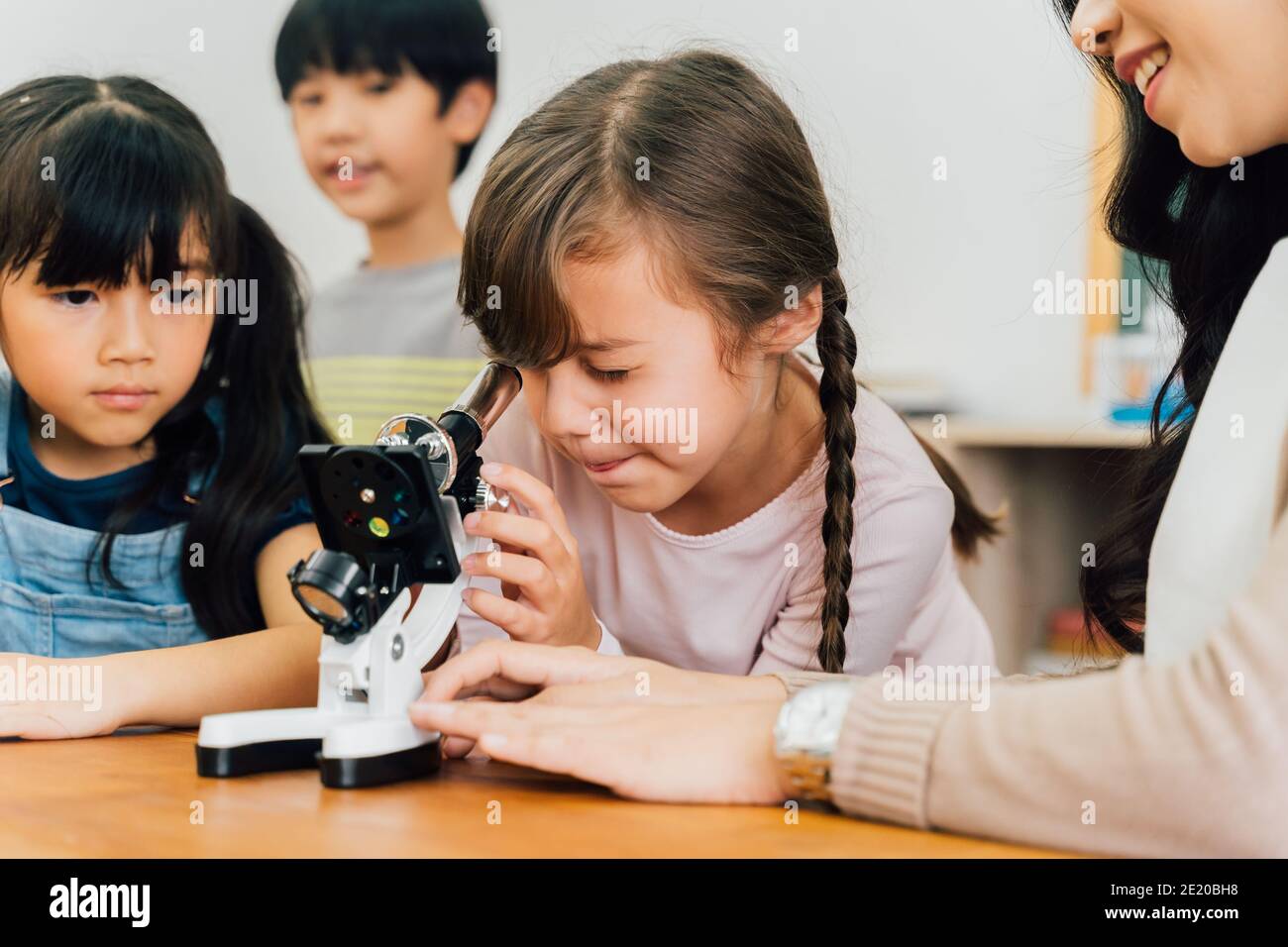 Young woman showing multiethnic children microscope in science class