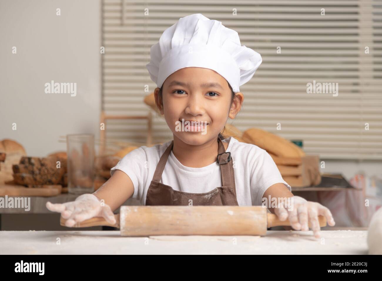 https://c8.alamy.com/comp/2E20C3J/asian-little-girl-uses-a-rolling-pin-to-knead-the-dough-to-make-a-homemade-bakery-the-kid-wore-a-white-chef-hat-brown-apron-with-a-smile-2E20C3J.jpg