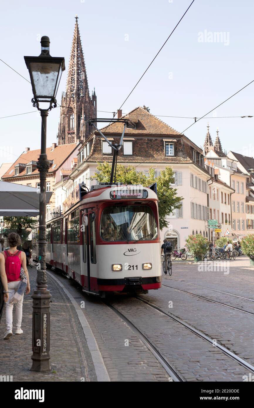 A vintage-style number 1 tram toward the Musikhochschule on Oberlinden in Freiburg im Breisgau, Germany, with the spire of the minster (cathedral). Stock Photo