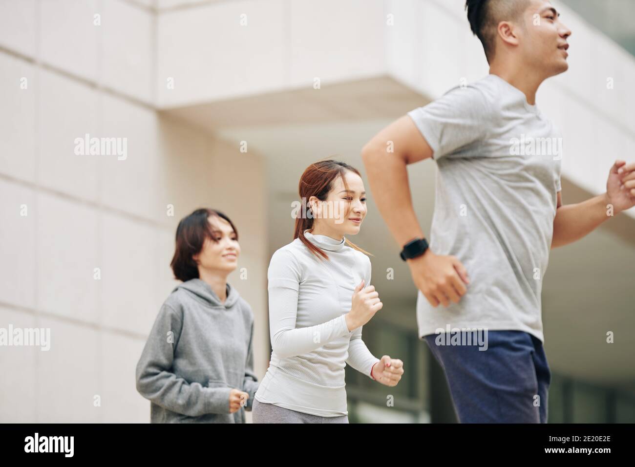 Pretty young Vietnamese woman running outdoors with group of friends to