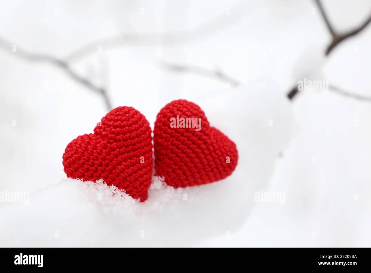 Valentine hearts in winter forest, cold weather. Two red knitted hearts on snow covered branch, symbol of romantic love, background for holiday Stock Photo