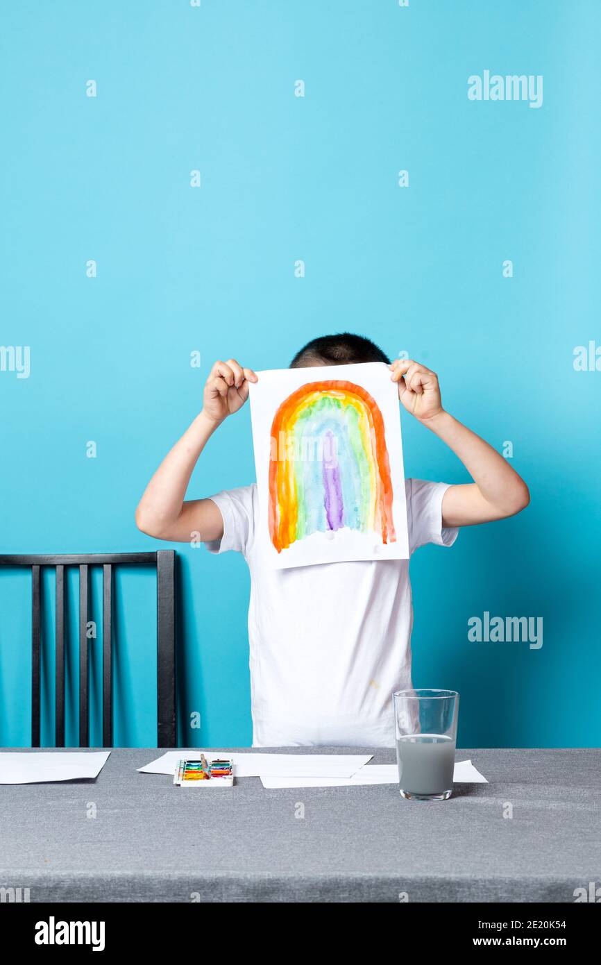 Children's creativity. Mock-up, a boy shows his rainbow drawing painted in watercolor on a4 sheet on a blue background Stock Photo