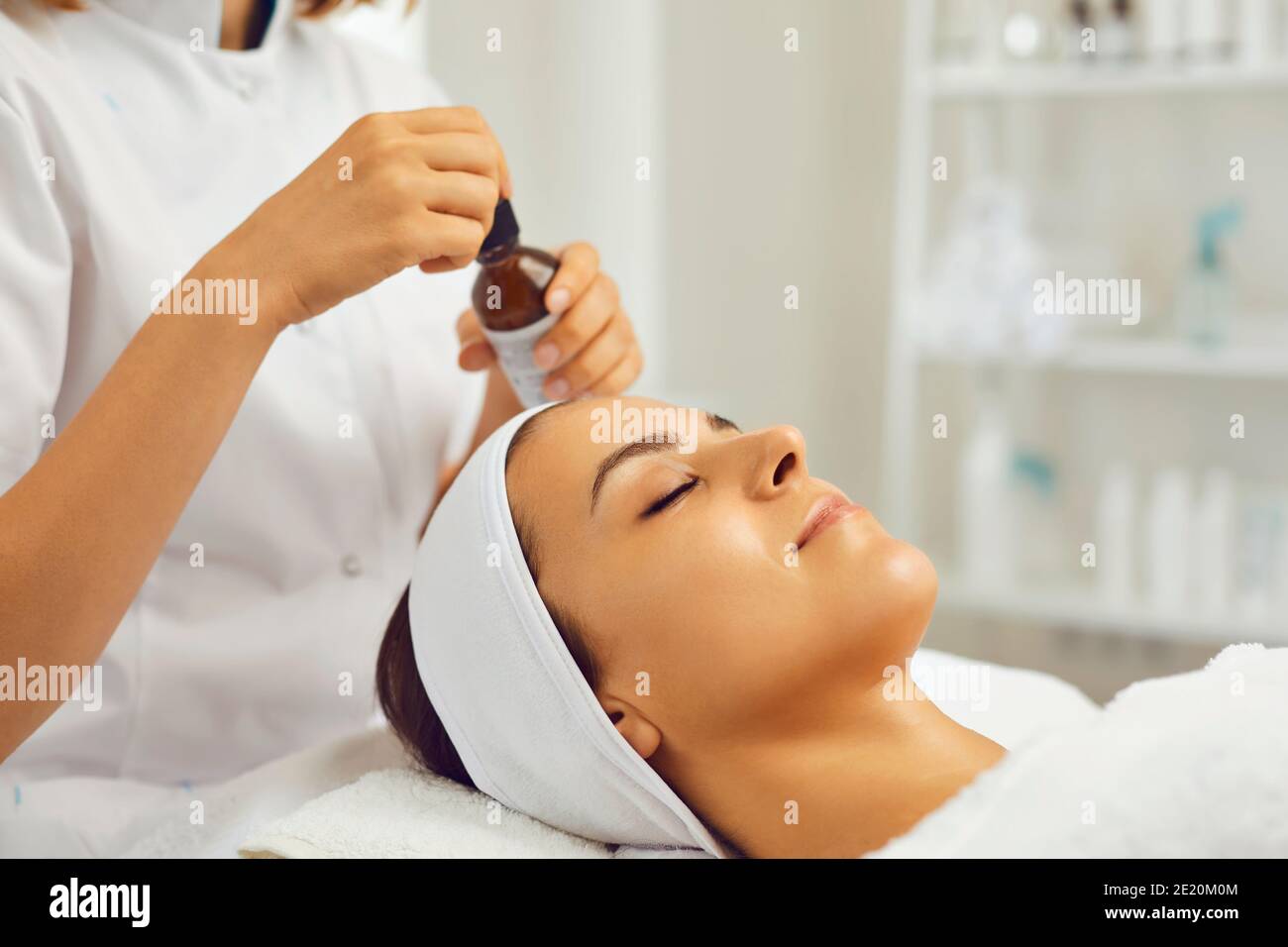 Hands of therapist ready to put nourishing skin oil to young womans face during skincare procedure Stock Photo