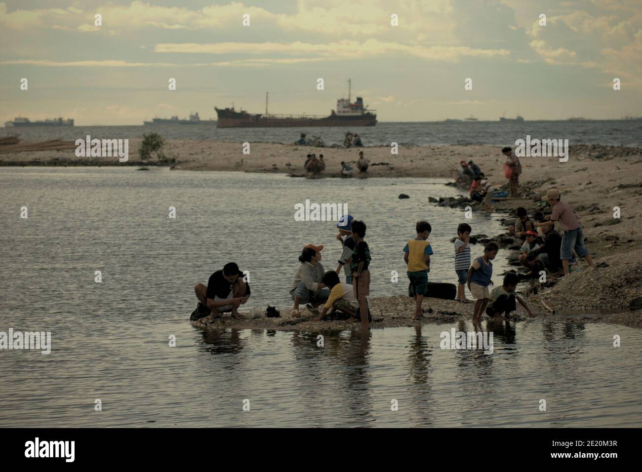 People having recreational time in Cilincing beach, on the coastal area of Jakarta, Indonesia. Port of Jakarta's traffics can be seen in the distance. Archival photo (2008). Stock Photo