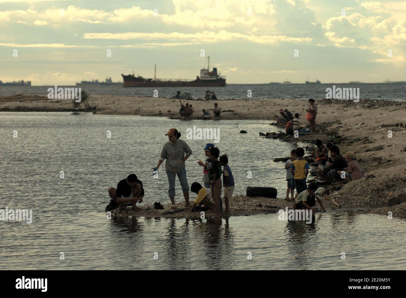 People having a recreational time on Cilincing beach in the coastal area of Jakarta, with a ship can be seen in the distance heading to the Port of Jakarta. Jakarta, Indonesia. Archival photo (2008). Stock Photo