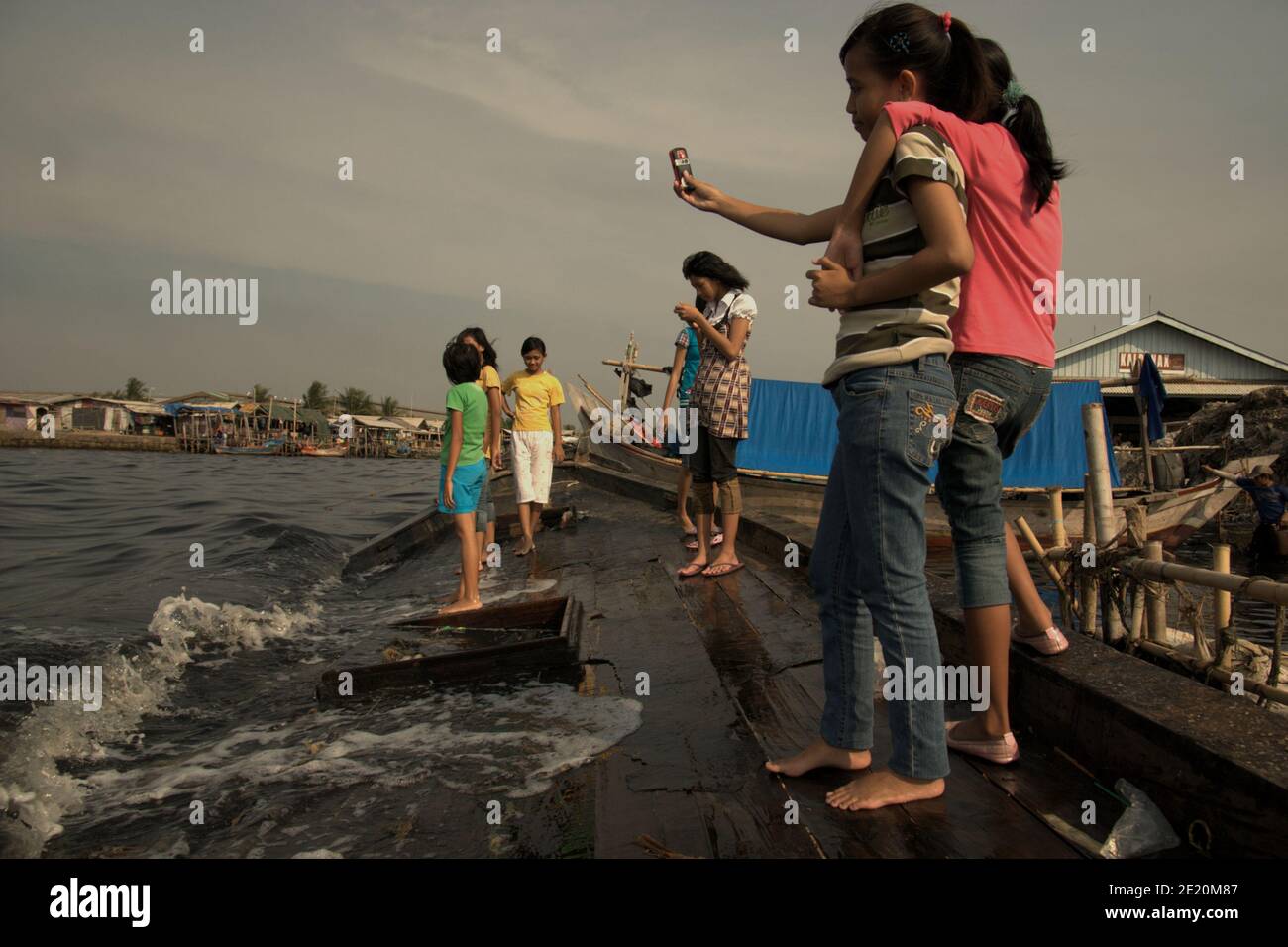 Teenagers taking selfie photo with mobile phone camera, as they are having a leisure time on a broken boat tied to the beach in the fishing village of Cilincing, on the coastal area of Jakarta, Indonesia. Archival photo (2008). © Reynold Sumayku Stock Photo