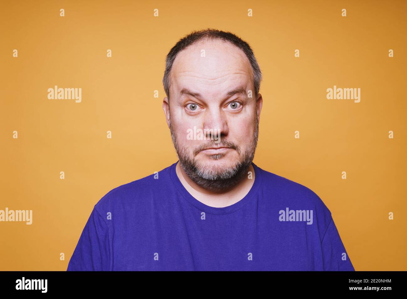 portrait of mid adult man with dumbfounded look on his face against orange color studio background - bewildered facial expression Stock Photo