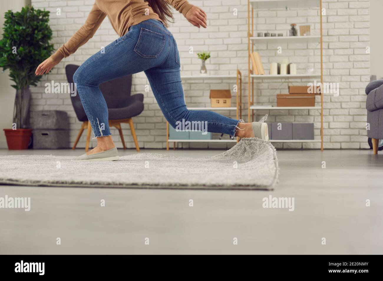 Clumsy woman stumbles on the rug in the living-room and falls down on the floor Stock Photo