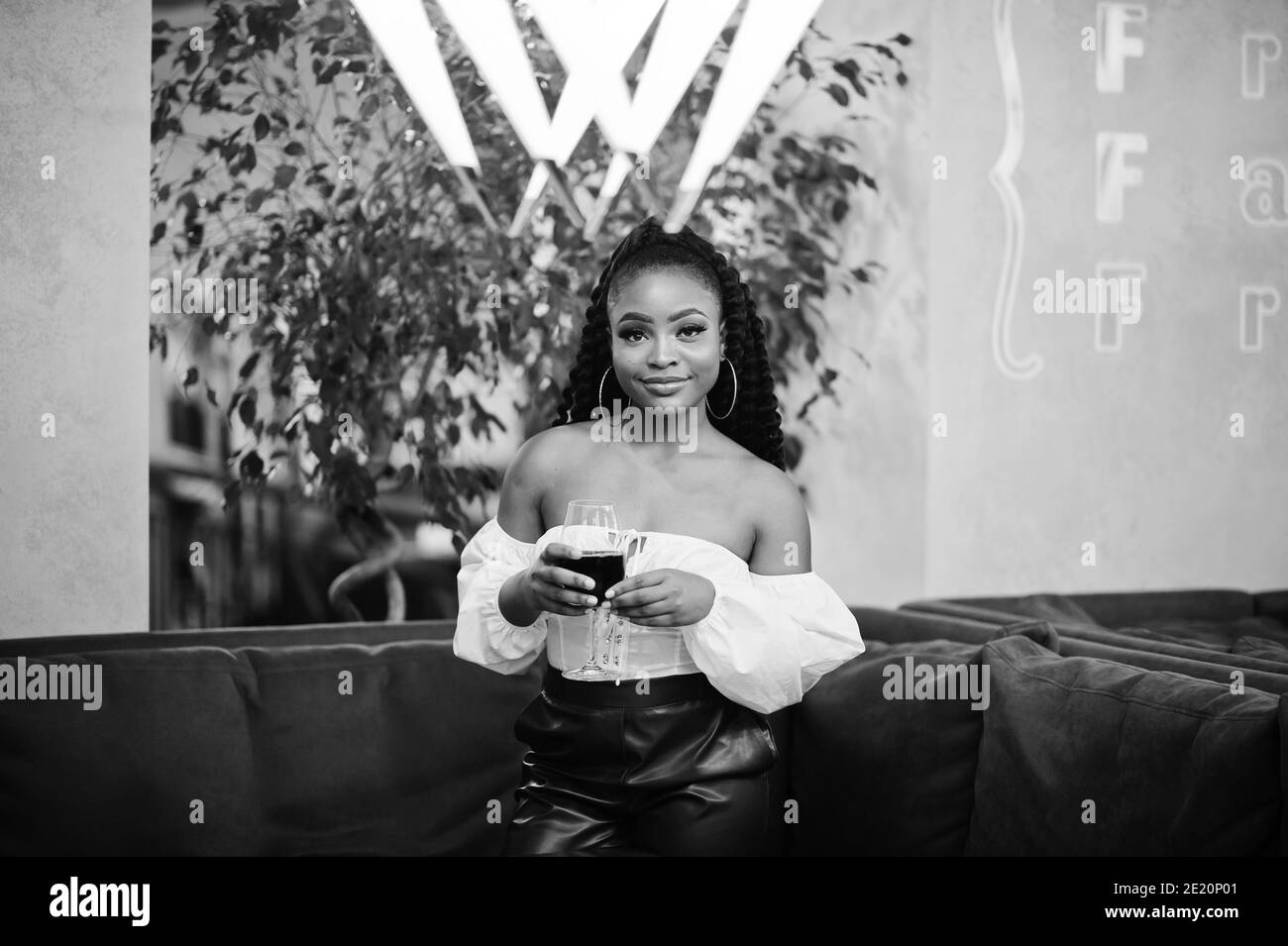 Beautiful african american woman in white blouse and red leather pants pose at restaurant with glass of wine. Stock Photo