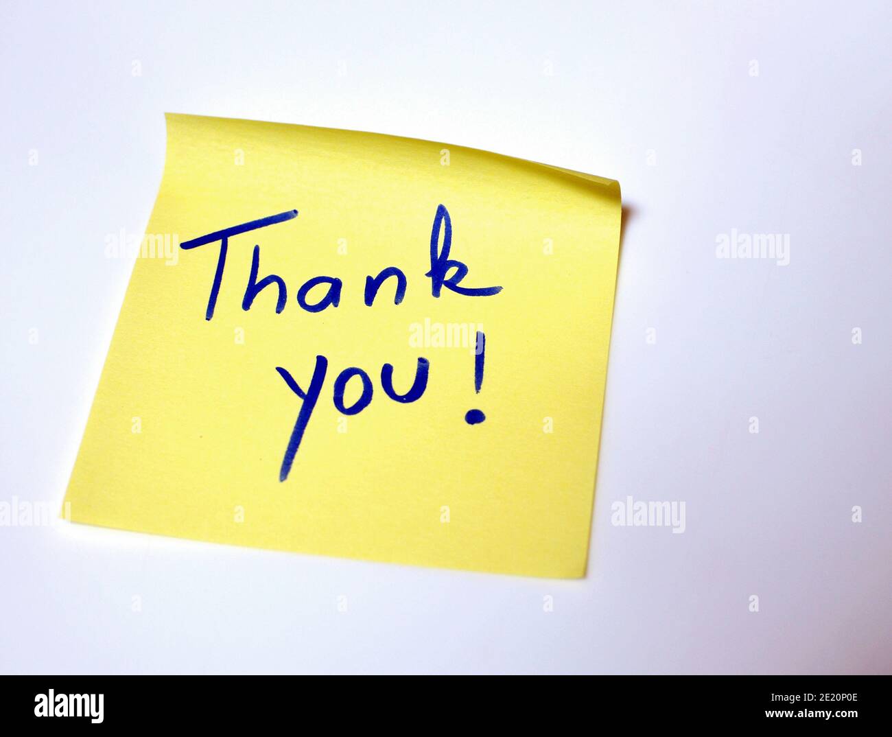 The sentence Thank you written by hand on a yellow post it and put on the white table Stock Photo