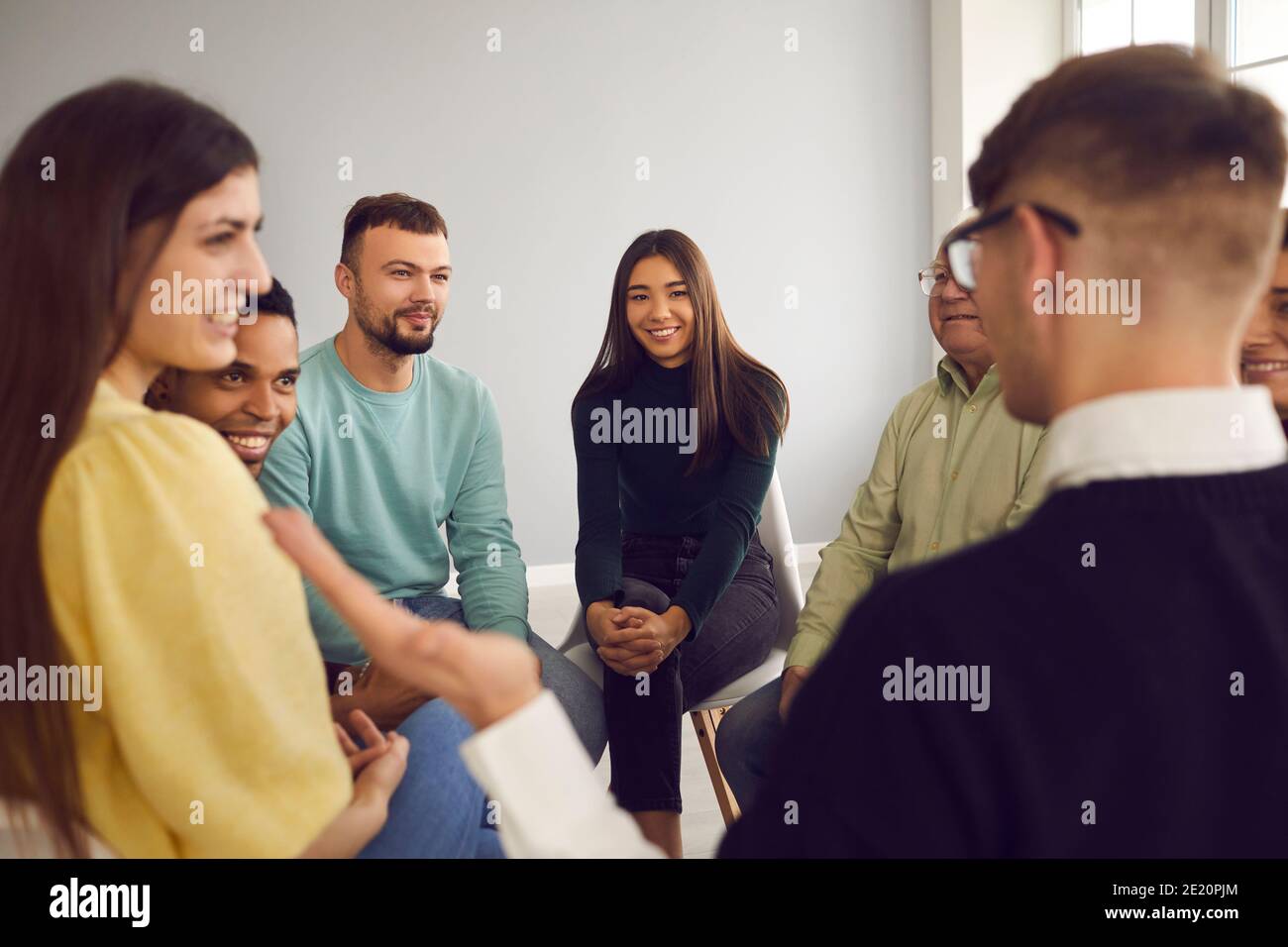 Multiracial people sit in a circle and listen to the story of the participant of the meeting. Stock Photo