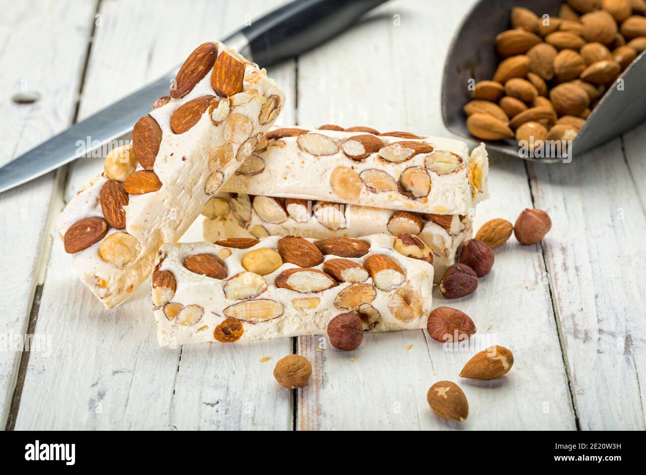 Turron blocks with almonds and hazelnuts on rustic wooden table with knife and shovel Stock Photo