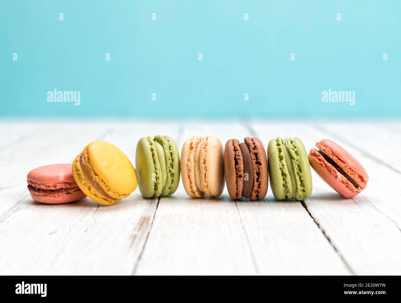 Row of colorful macarons on rustic white table. Delicious French pastry assortment closeup. Stock Photo