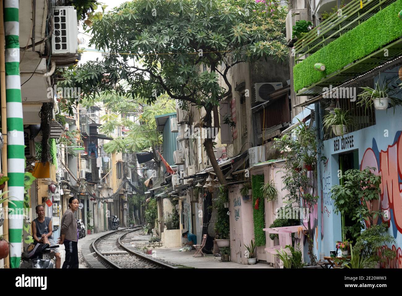 People socializing along a railway line running between buildings in Hanoi Stock Photo