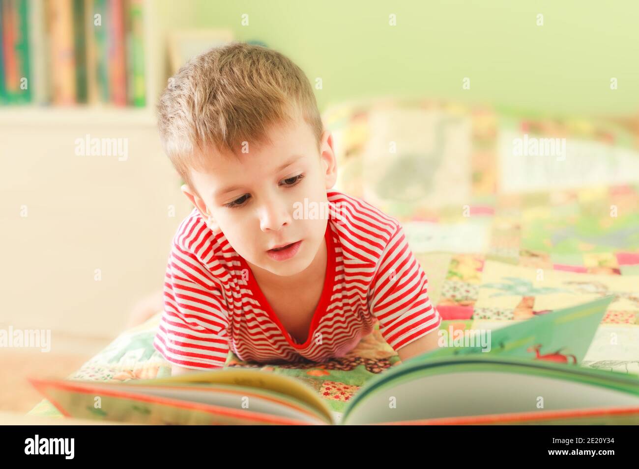 Cute little boy reading alphabet book while laying on bed. Child looks