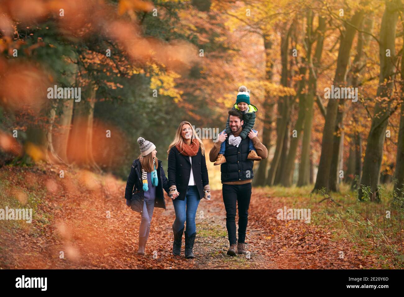 Family Walking Along Autumn Woodland Path With Father Carrying Son On ...