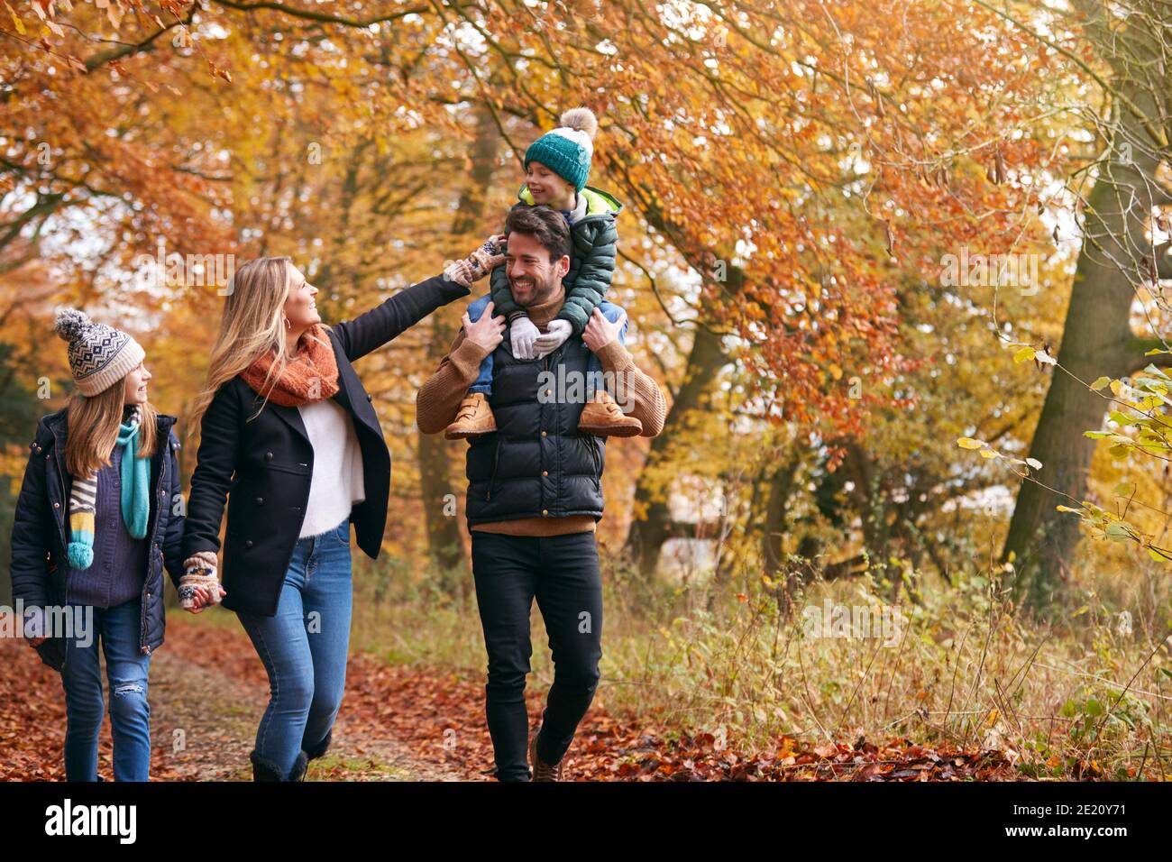 Family Walking Along Autumn Woodland Path With Father Carrying Son On ...