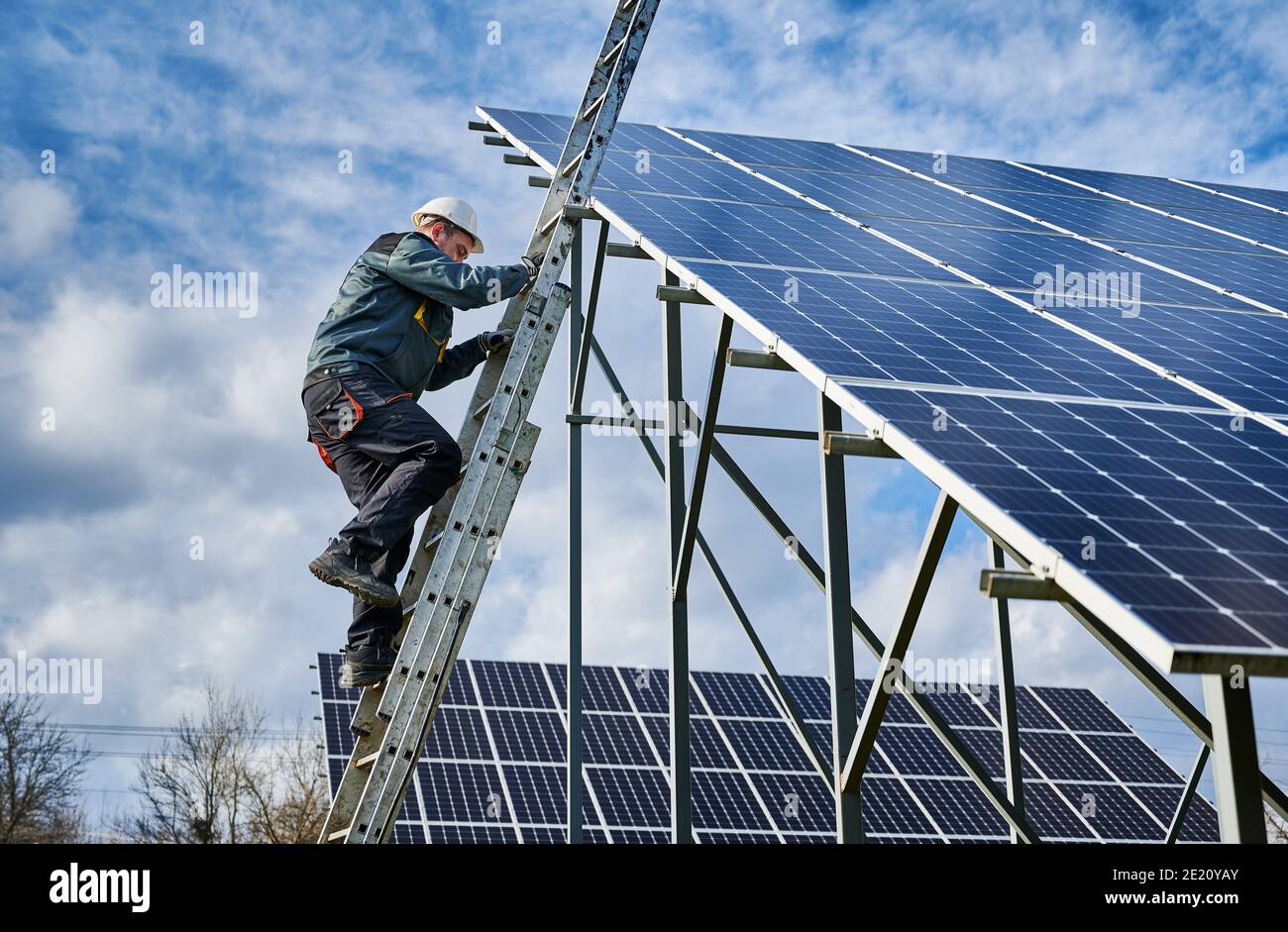 Technician getting down the ladder after installing photovoltaic solar panels on a sunny day. Renewable energy resource. Concept of alternative energy and power sustainable resources. Stock Photo