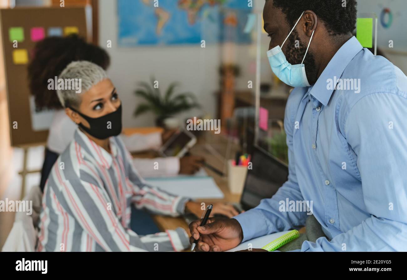 Young people in co-working creative space wearing surgical mask and keeping social distance to avoid corona virus spread Stock Photo