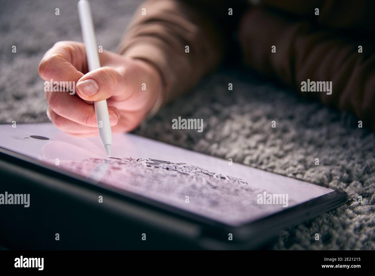 Close Up Of Woman Drawing On Digital Tablet Using Stylus Pen Lying On Carpet At Home Stock Photo