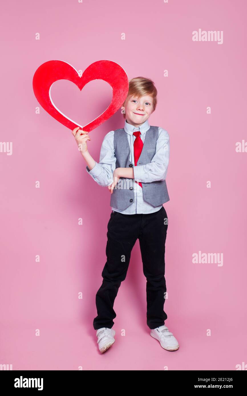 Valentines day. Smiling stylish little boy posing with heart on pink