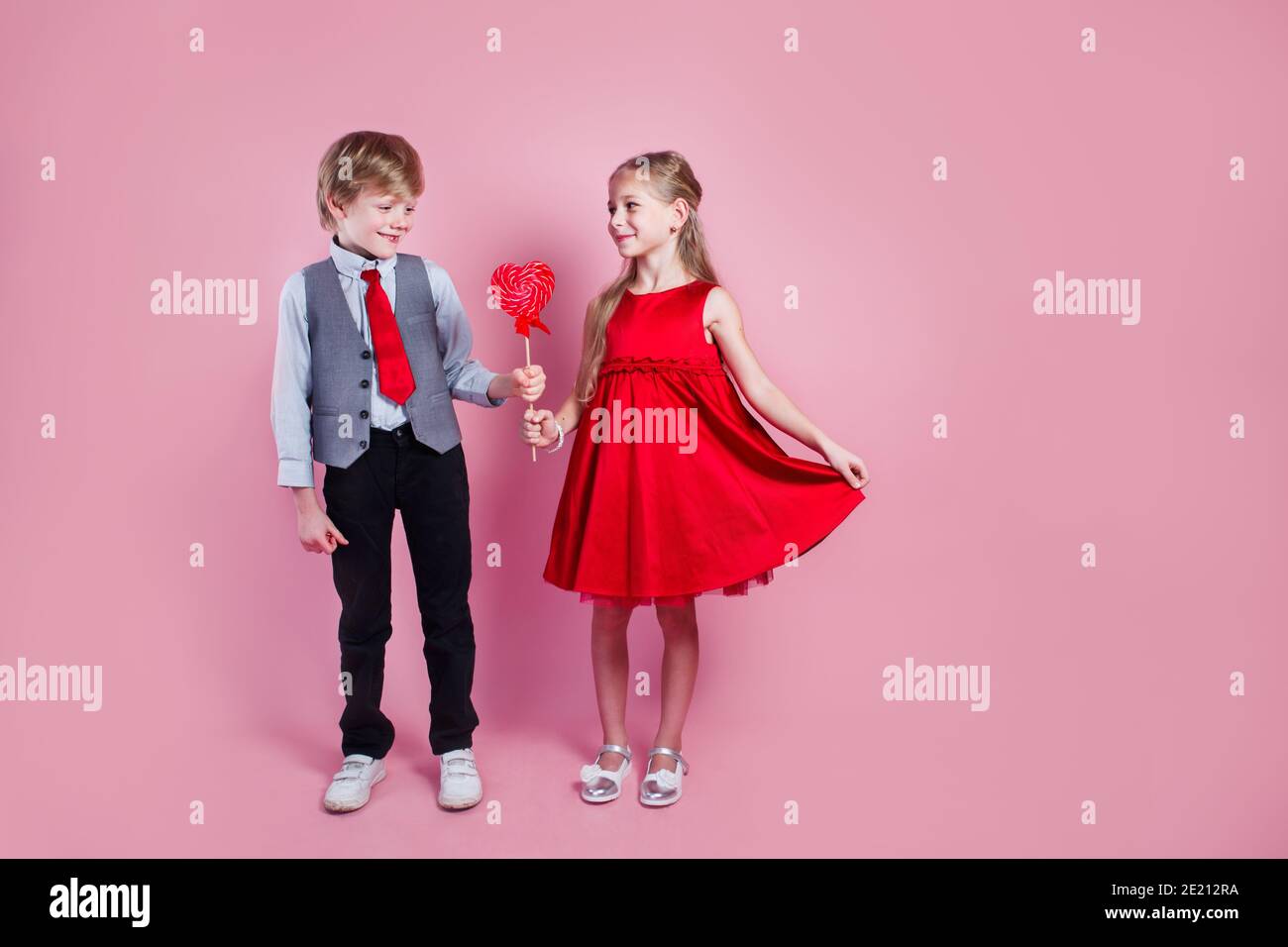 Valentine's day concept. Little boy and girl with candy red lollipop in heart shape. Beautiful children eat sweets. Stock Photo