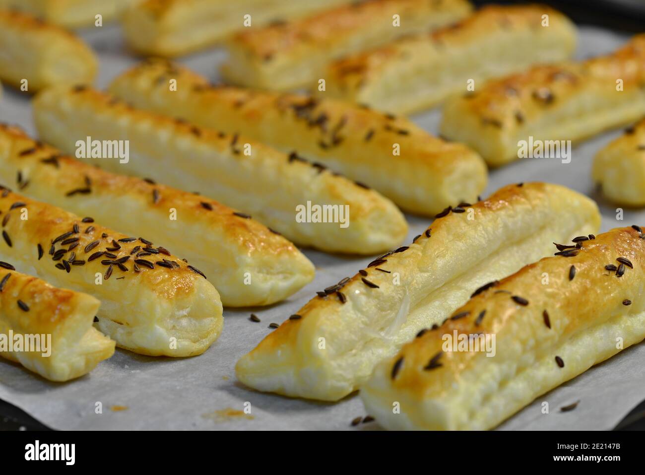Baked salty sticks with salt and cumin. Golden baked savory pastry. Home baking appetizers. Crispy savory pastry on a baking sheet. Stock Photo