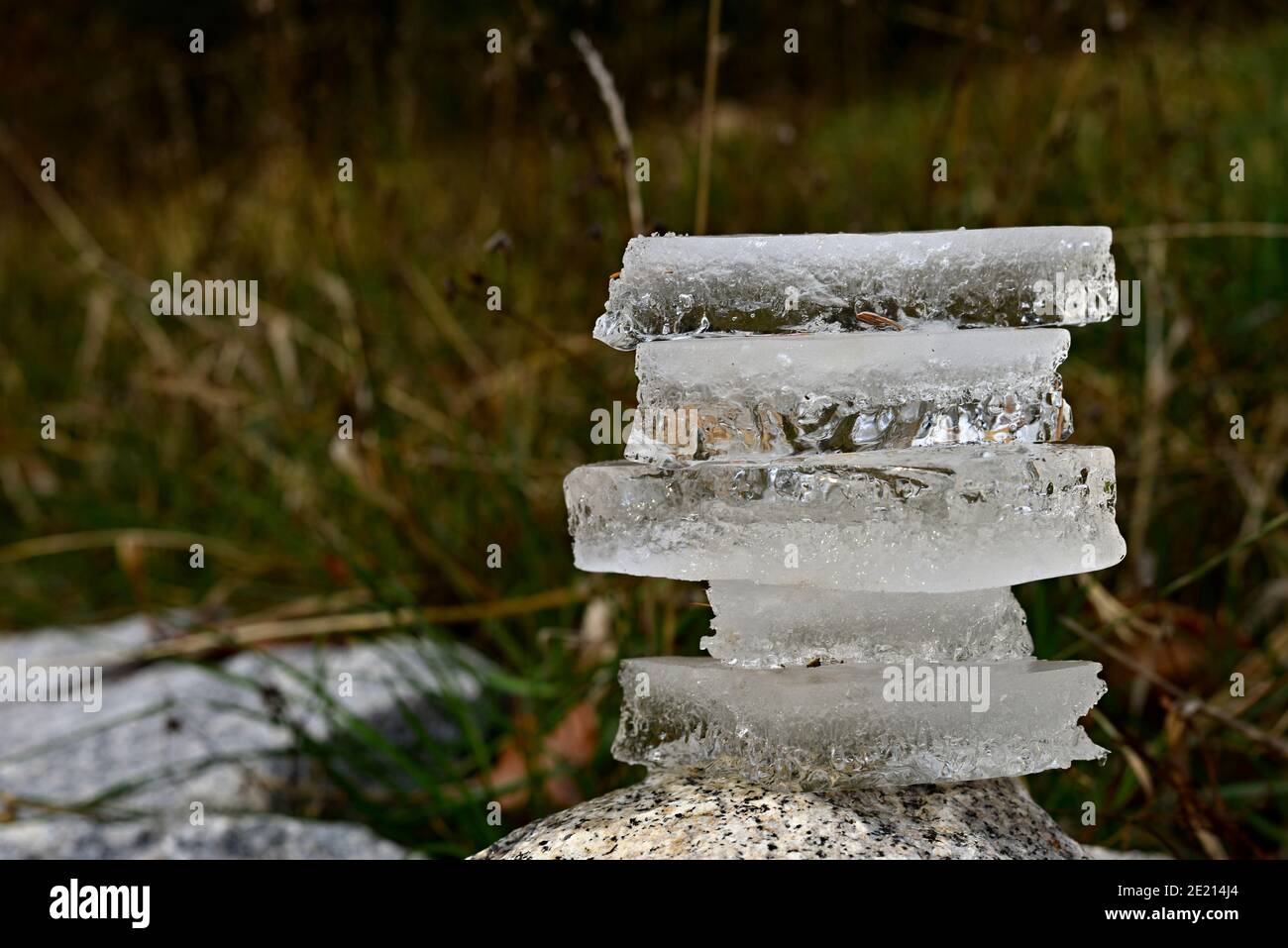 Ice stacked on top of each other. Balancing ice pieces into an mound. Pieces of ice stacked on a large boulder with winter green-brown grass in the ba Stock Photo