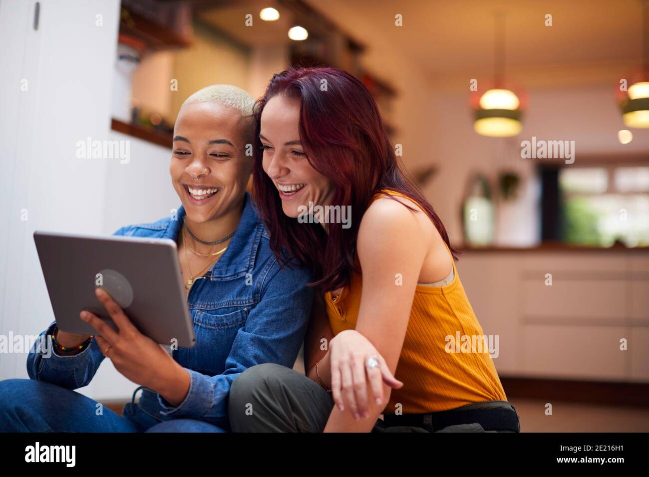 Loving Same Sex Female Couple Using Digital Tablet As They Relax At Home Together Stock Photo