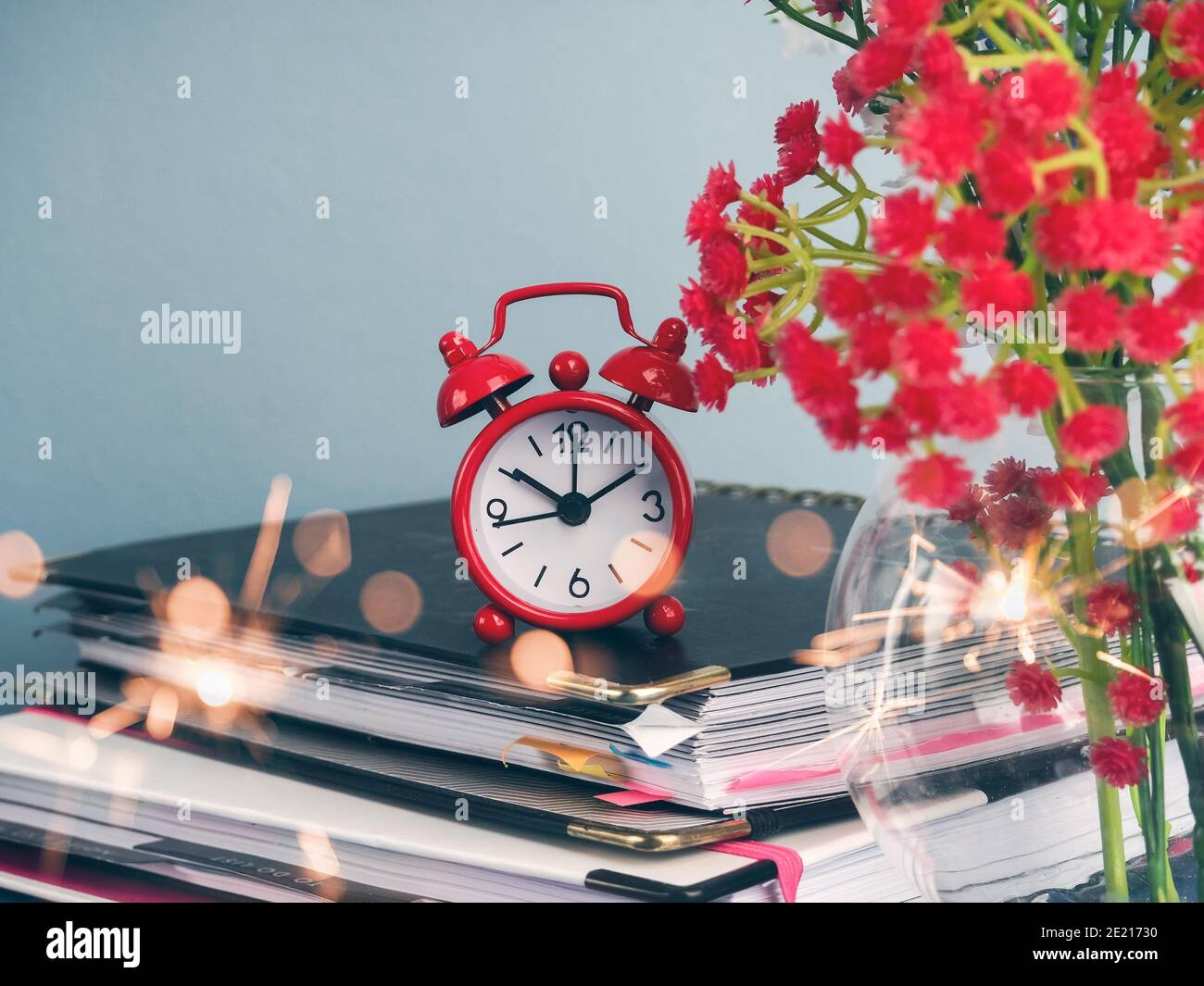 Alarm clock standing on table by stack of books against plain background Stock Photo