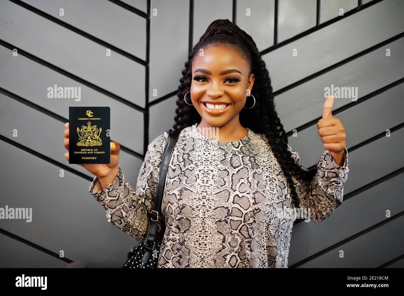 Close up portrait of young positive african american woman holding Trinidad and Tobago passport and thumbs up. Stock Photo