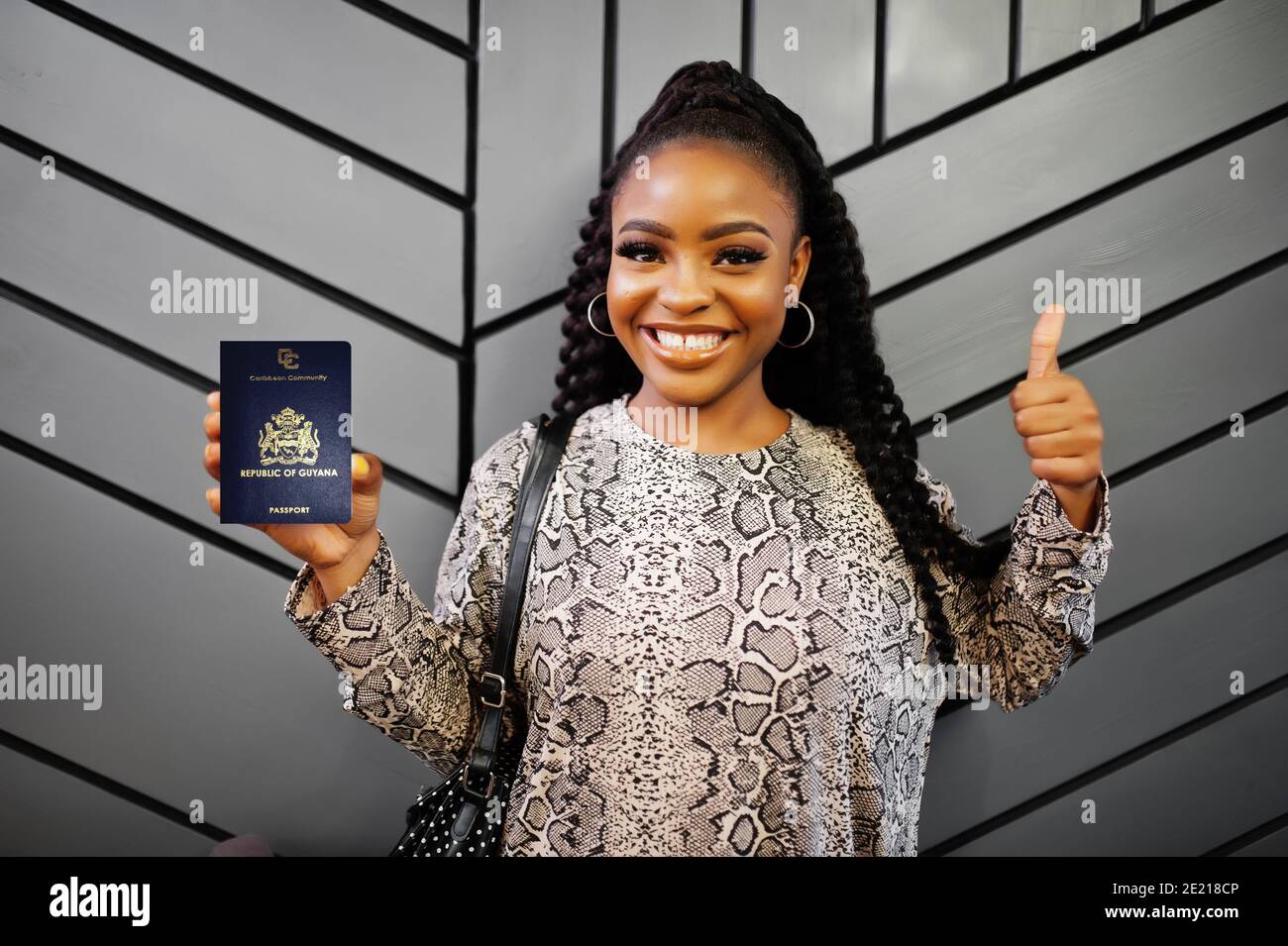 Close up portrait of young positive african american woman holding Guyana passport and thumbs up. Stock Photo