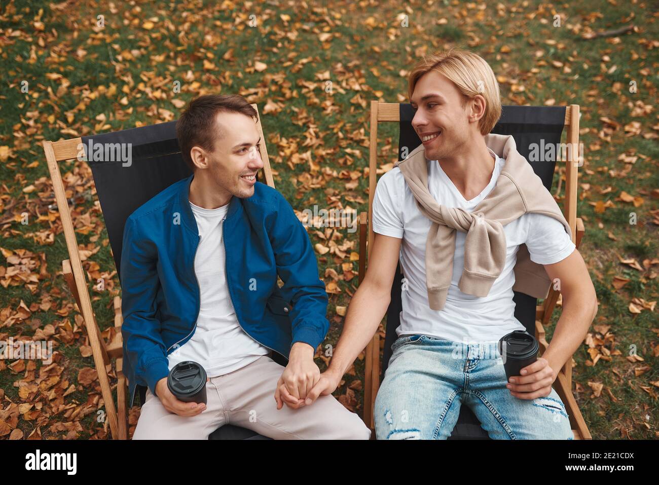 Loving gay couple sitting outdoors holding hands while enjoying coffee on a date.