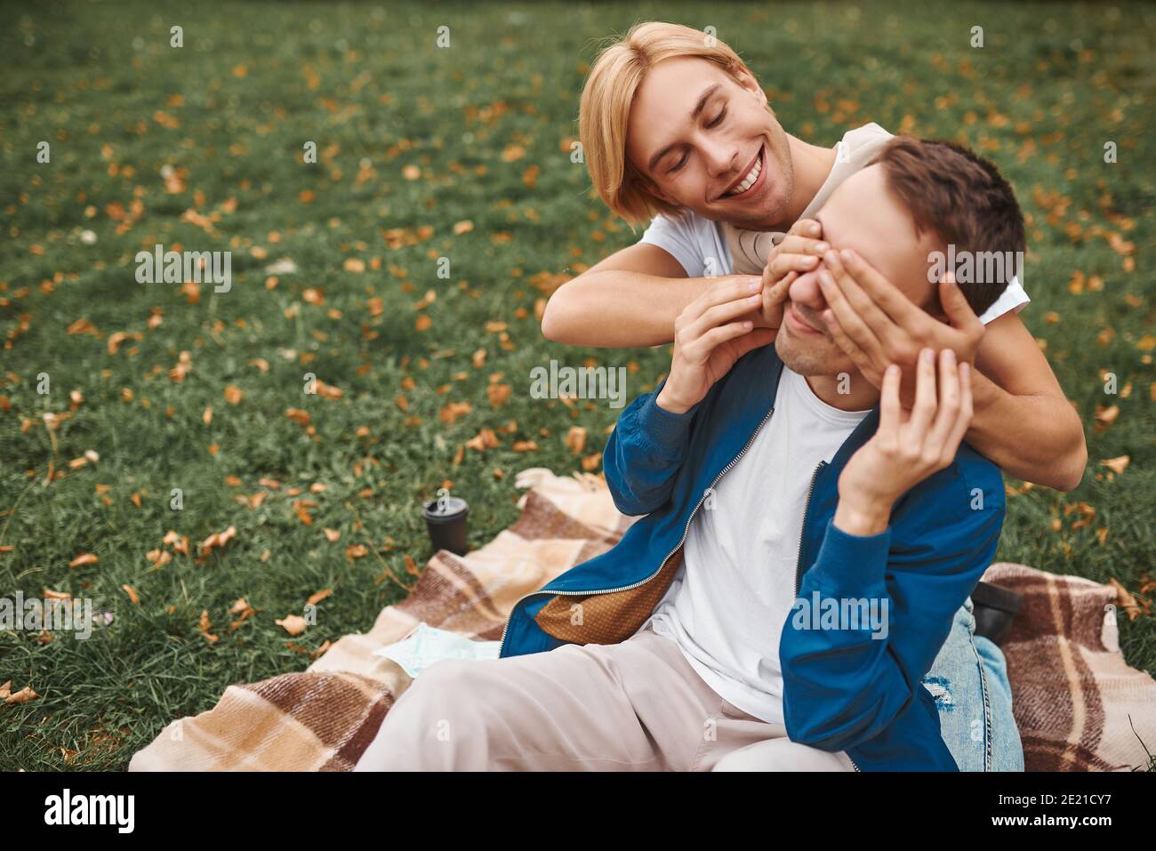 Loving gay couple having romantic date outdoors. Two handsome men sitting together on blanket in park. LGBT concept. Stock Photo
