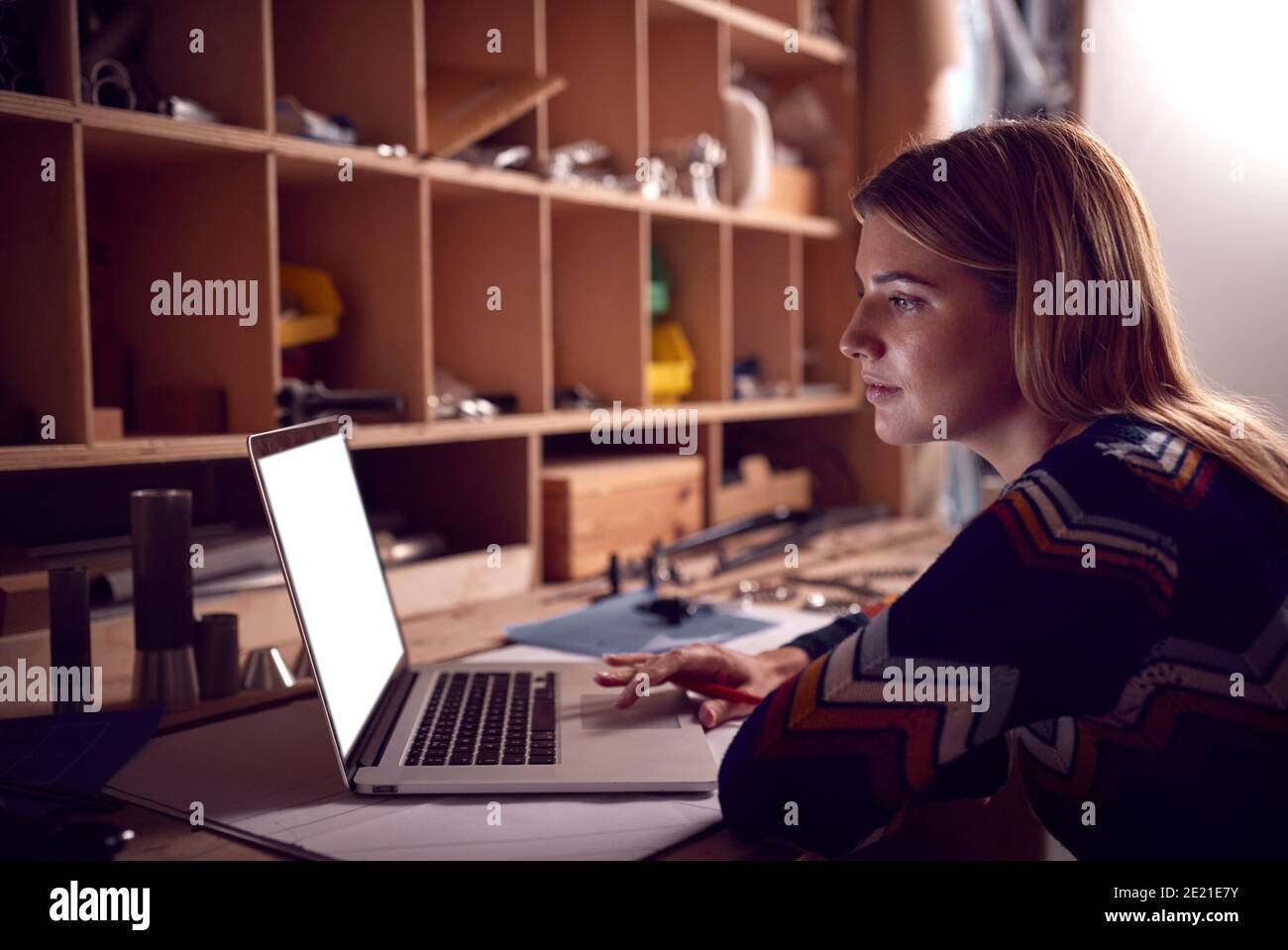 Female Business Owner Working Late In Carpentry Workshop Using Laptop Stock Photo