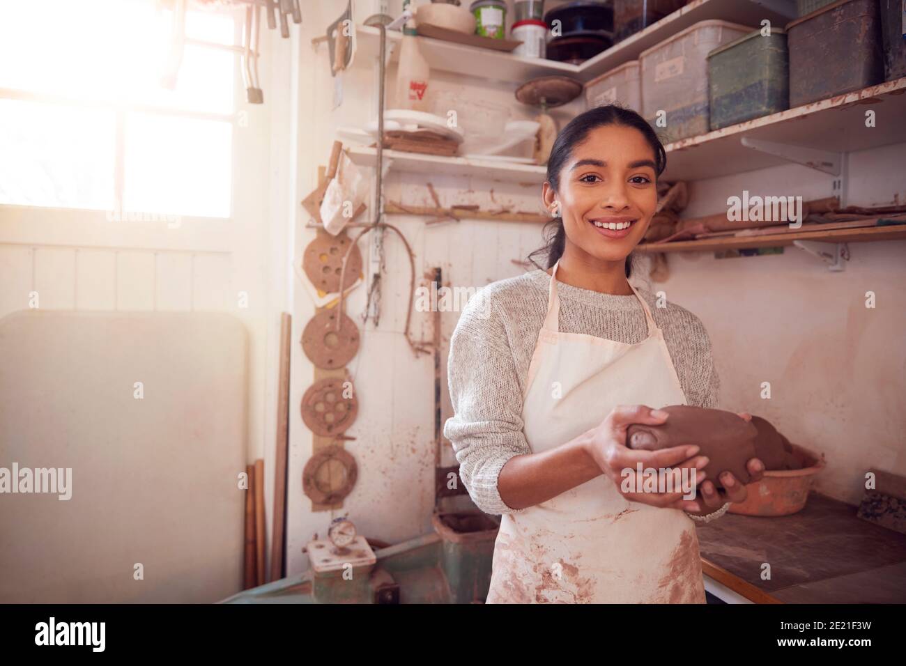 Portrait Of Female Potter Wearing Apron Holding Lump Of Clay In ...