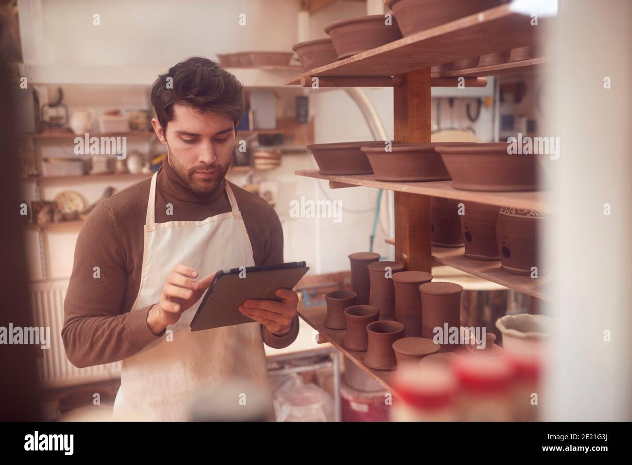 Male Potter In Ceramics Studio Checking Orders Using Digital Tablet Stock Photo