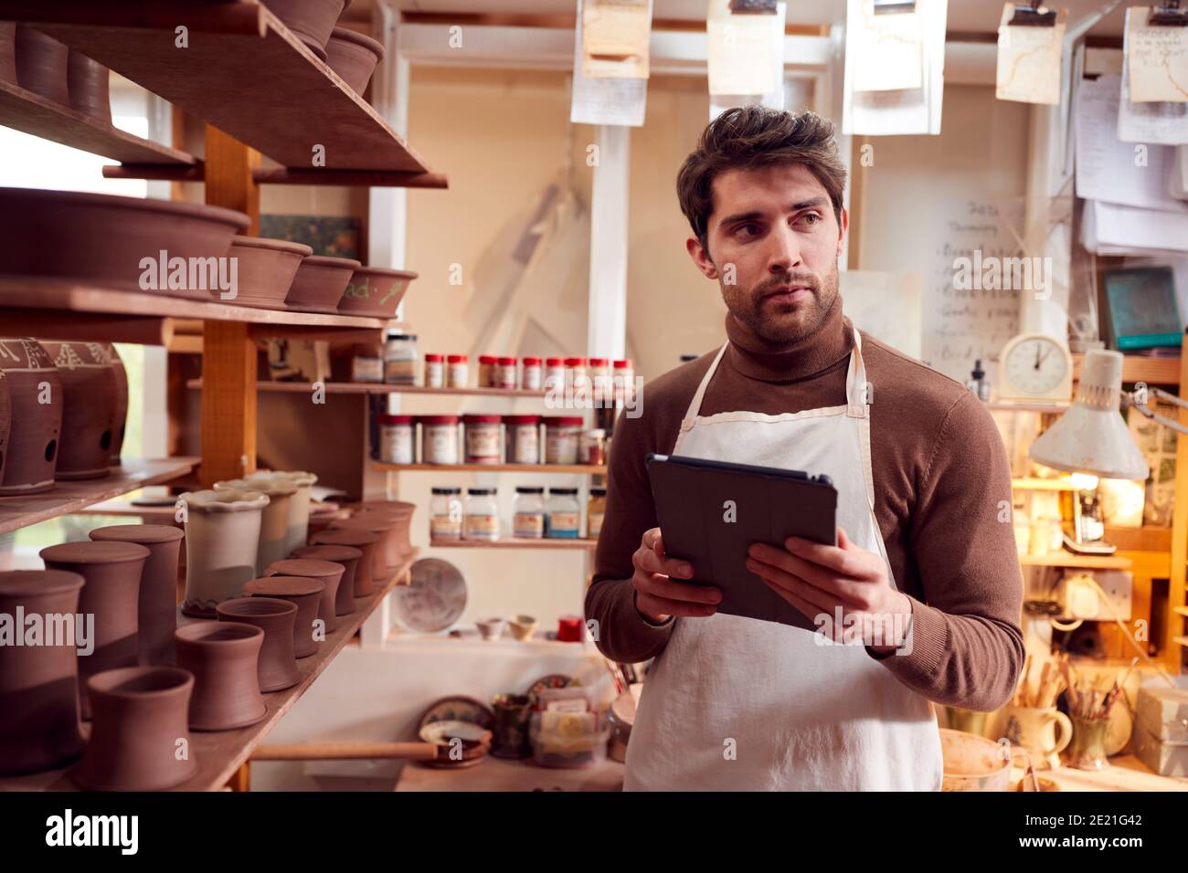 Male Potter In Ceramics Studio Checking Orders Using Digital Tablet Stock Photo