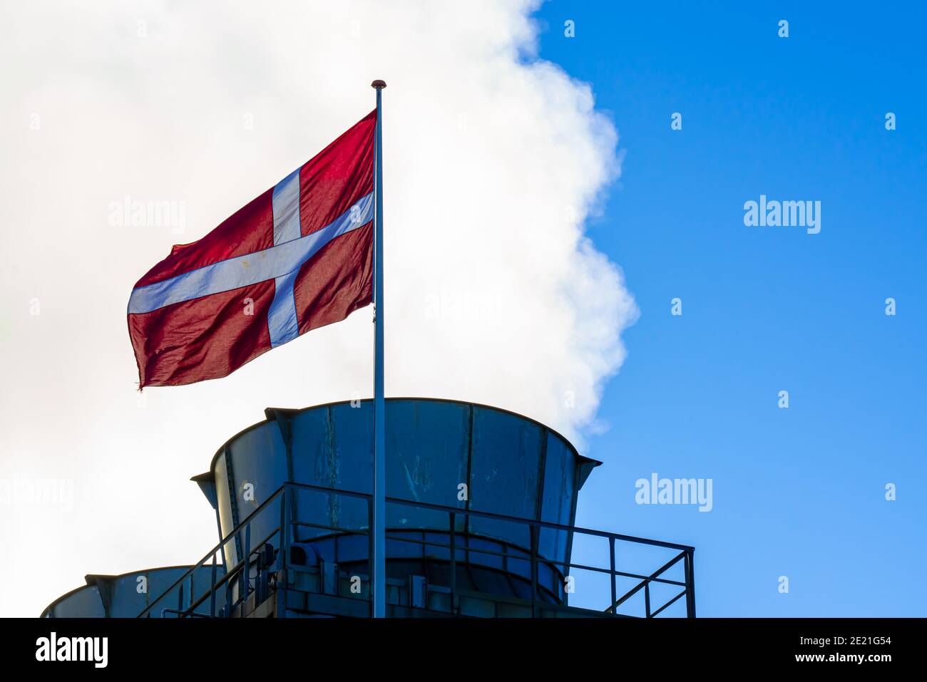 Smokestack with steam and smoke and a Danish flag in the foreground. Stock Photo