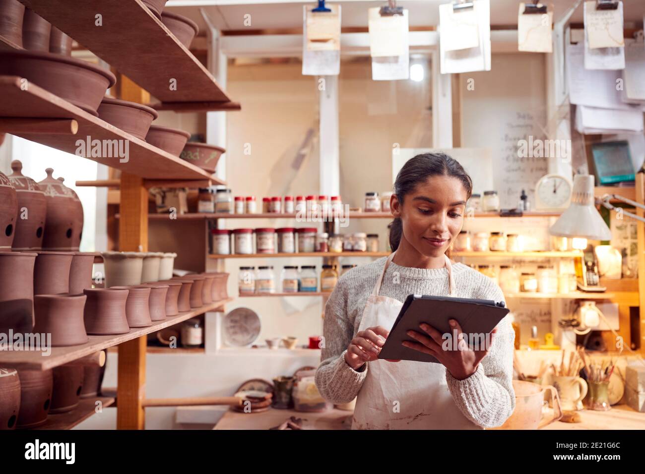 Female Potter In Ceramics Studio Checking Orders Using Digital Tablet Stock Photo