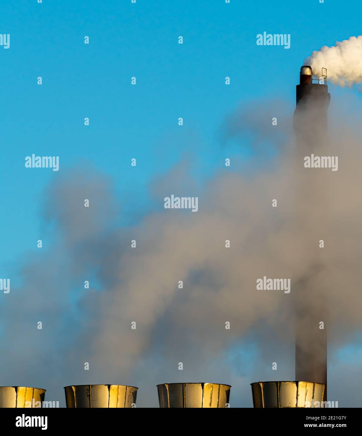 Industrial smoke stacks putting out steam and smoke on a clear blue sky. Stock Photo