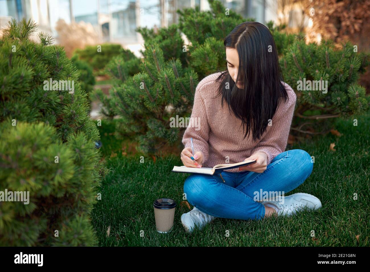 Confident female student writing messages at her daily planner and spending time outdoors in a warm day Stock Photo