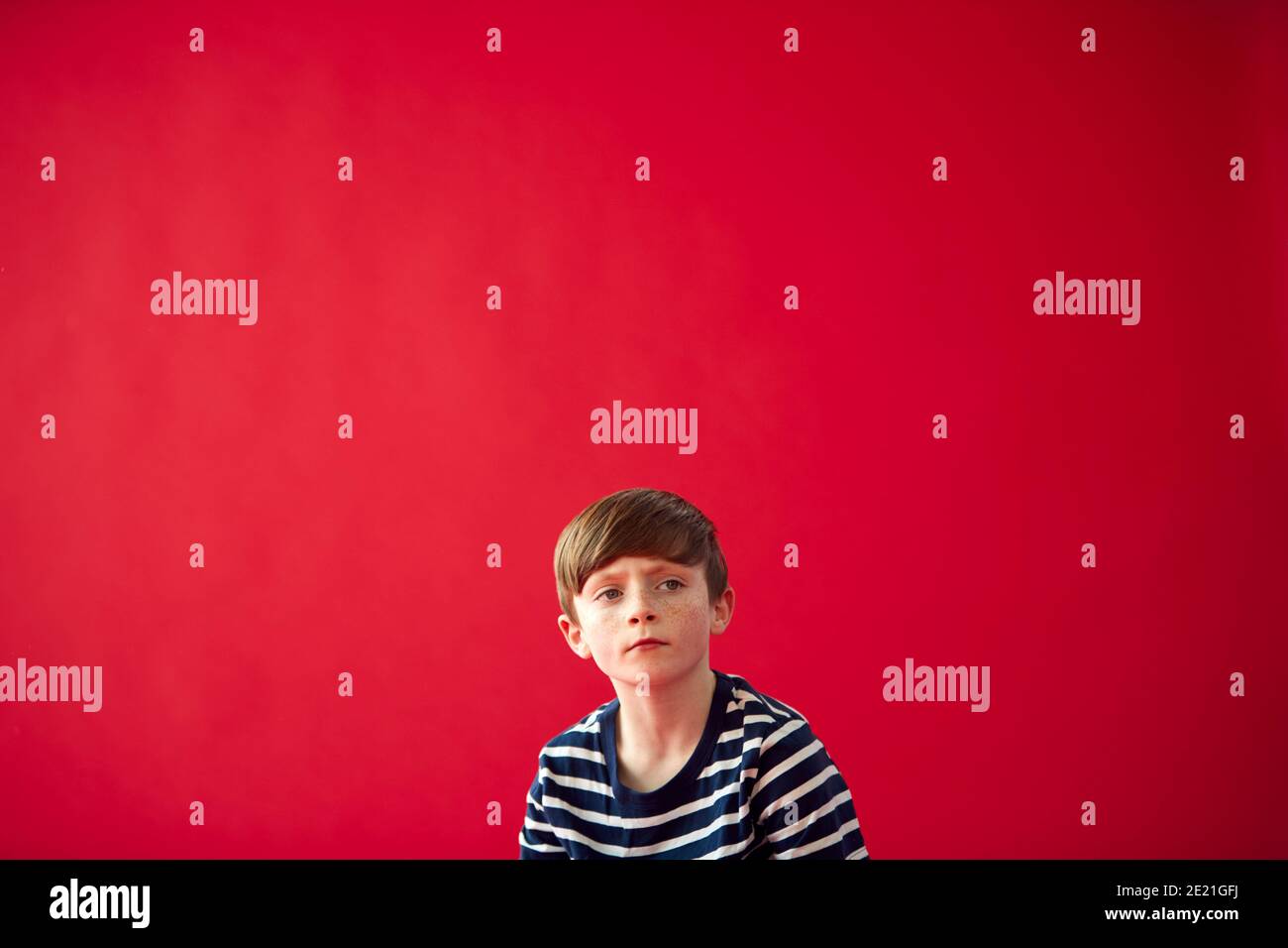 Portrait Of Thoughtful Young Boy Against Red Studio Background Stock Photo