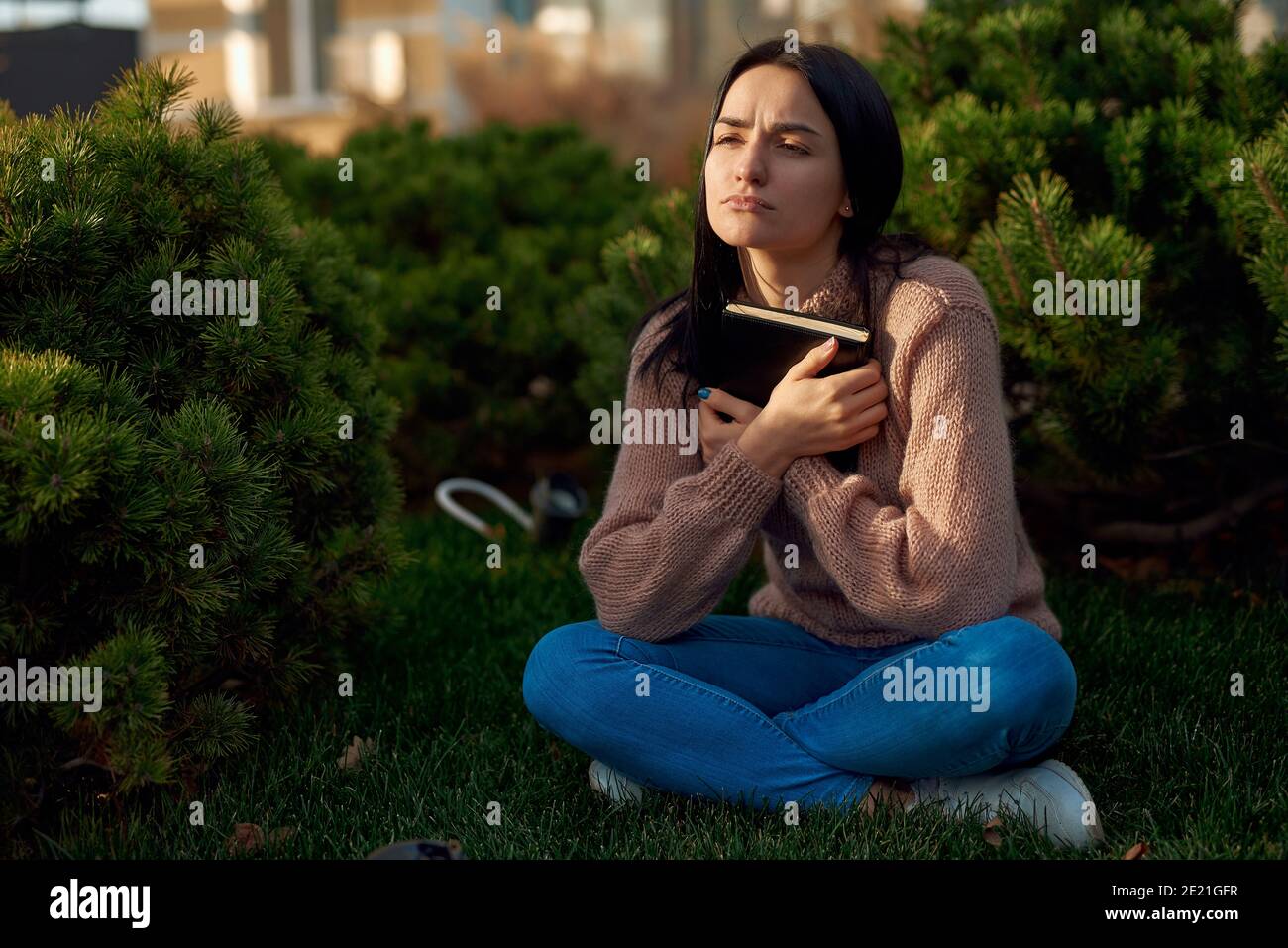 Young female in casual attire spending time alone in the foreyard while holding notebook Stock Photo