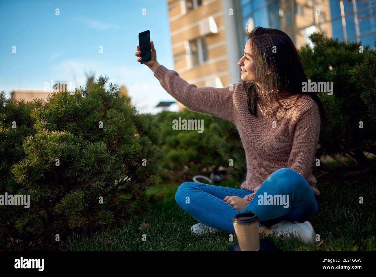Young beautiful dark-haired woman taking heartwarming picture of herself and sitting outdoors Stock Photo